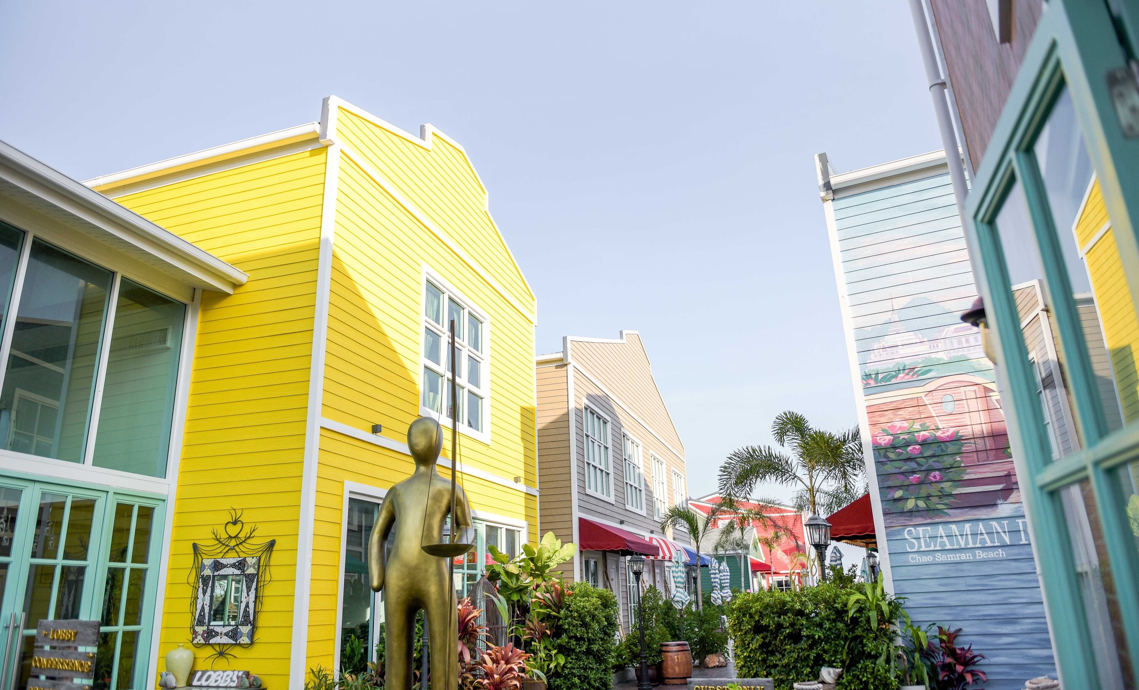 A colorful street with a yellow building, a blue building with a beach sign, and a green building with a sign that reads "STEMAN BEACH".
