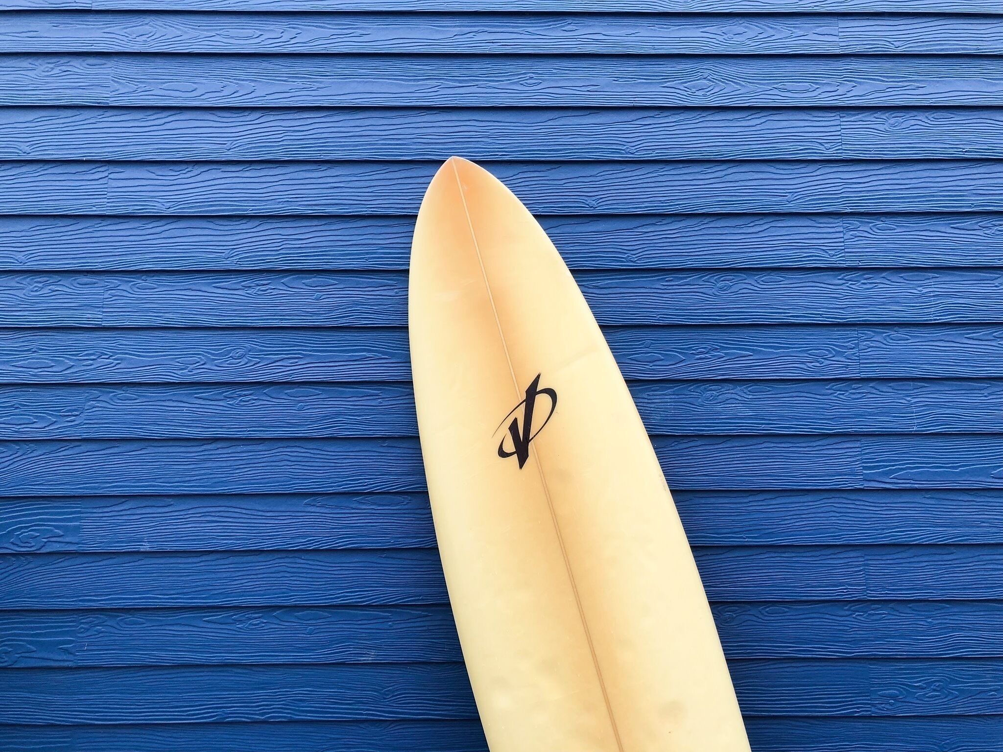 Une planche de surf ornée d’un logo, posée sur une surface en bois bleue.