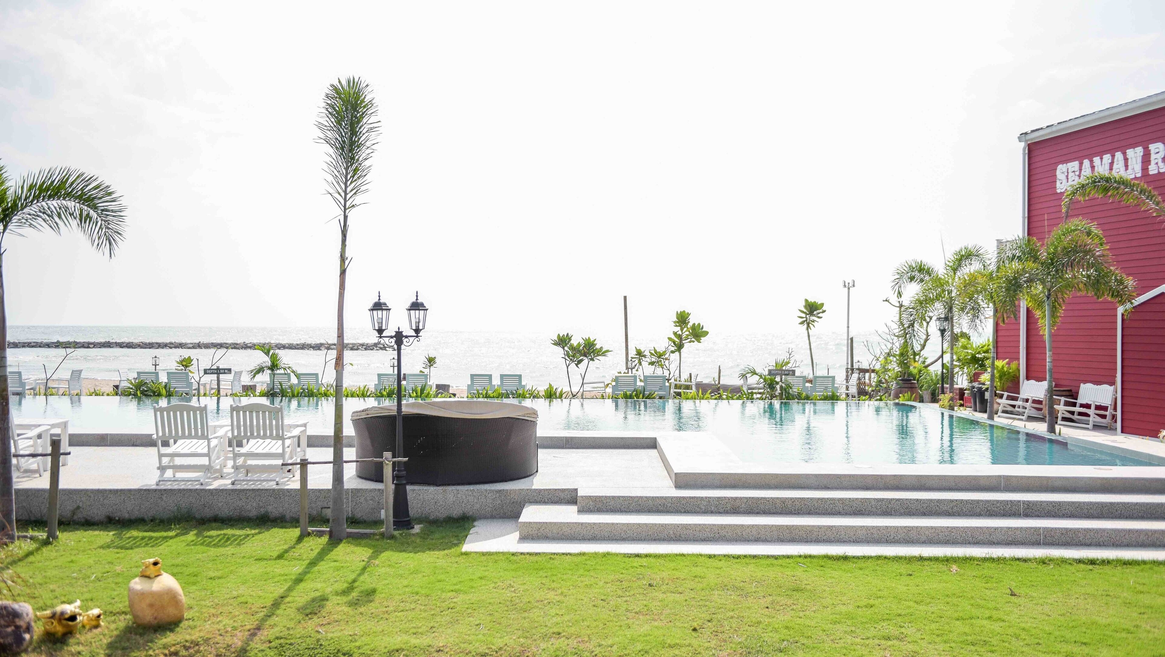 A pool area with lounge chairs, a red building labeled "SEAMAN R", and a view of the ocean.