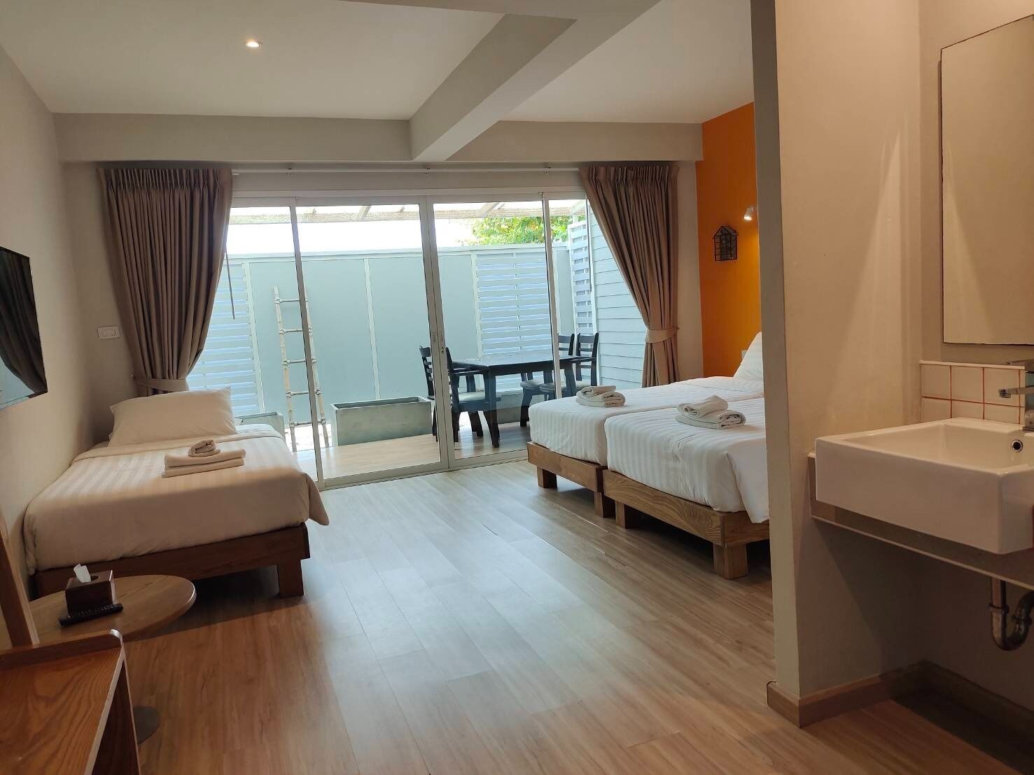 Hotelkamer met twee bedden, een kleine tafel, een stoel, een badkamer met een wastafel en een glazen schuifdeur naar een buitenruimte.