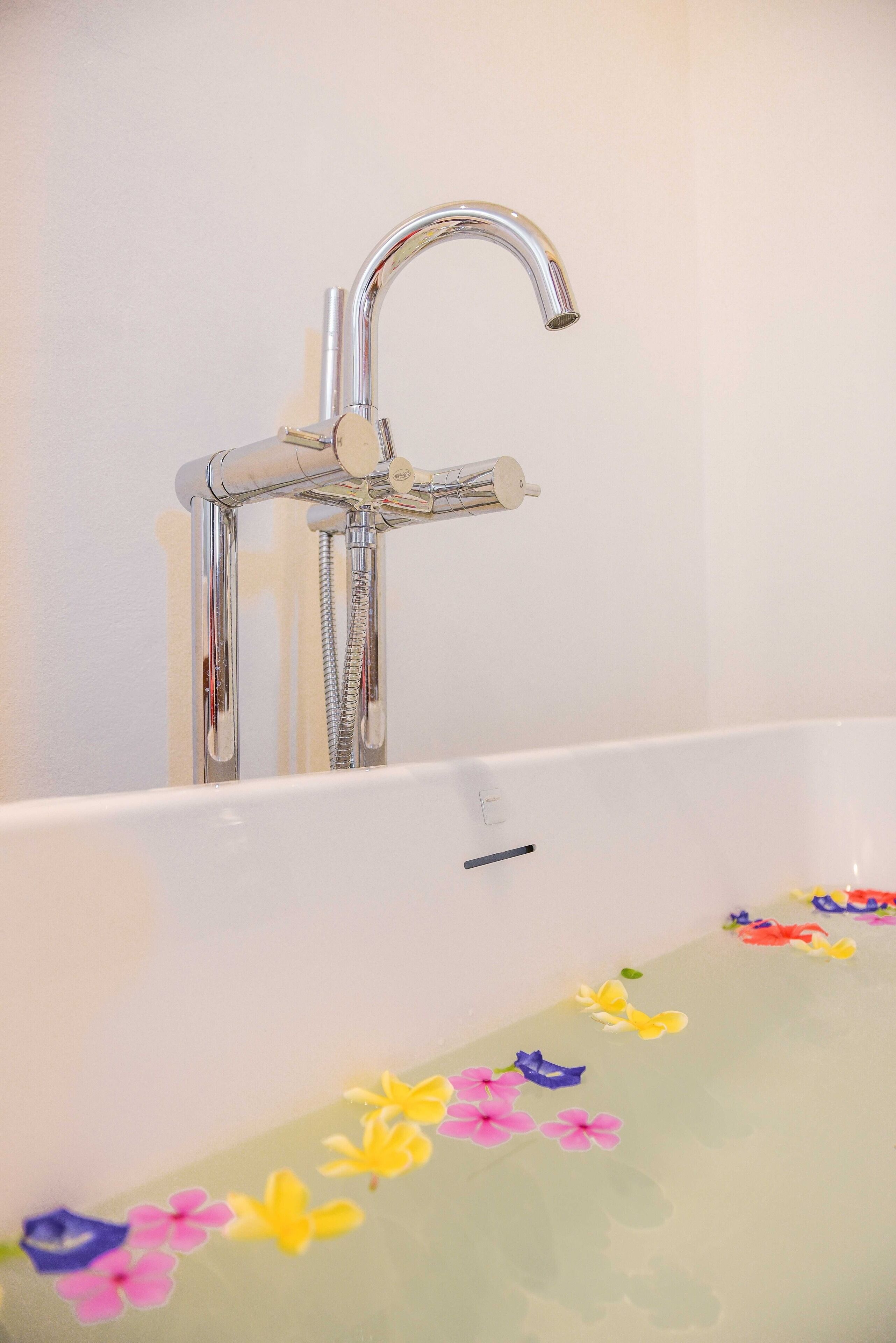 Una bañera con grifo de cromo y una alfombra de baño con motivos florales.