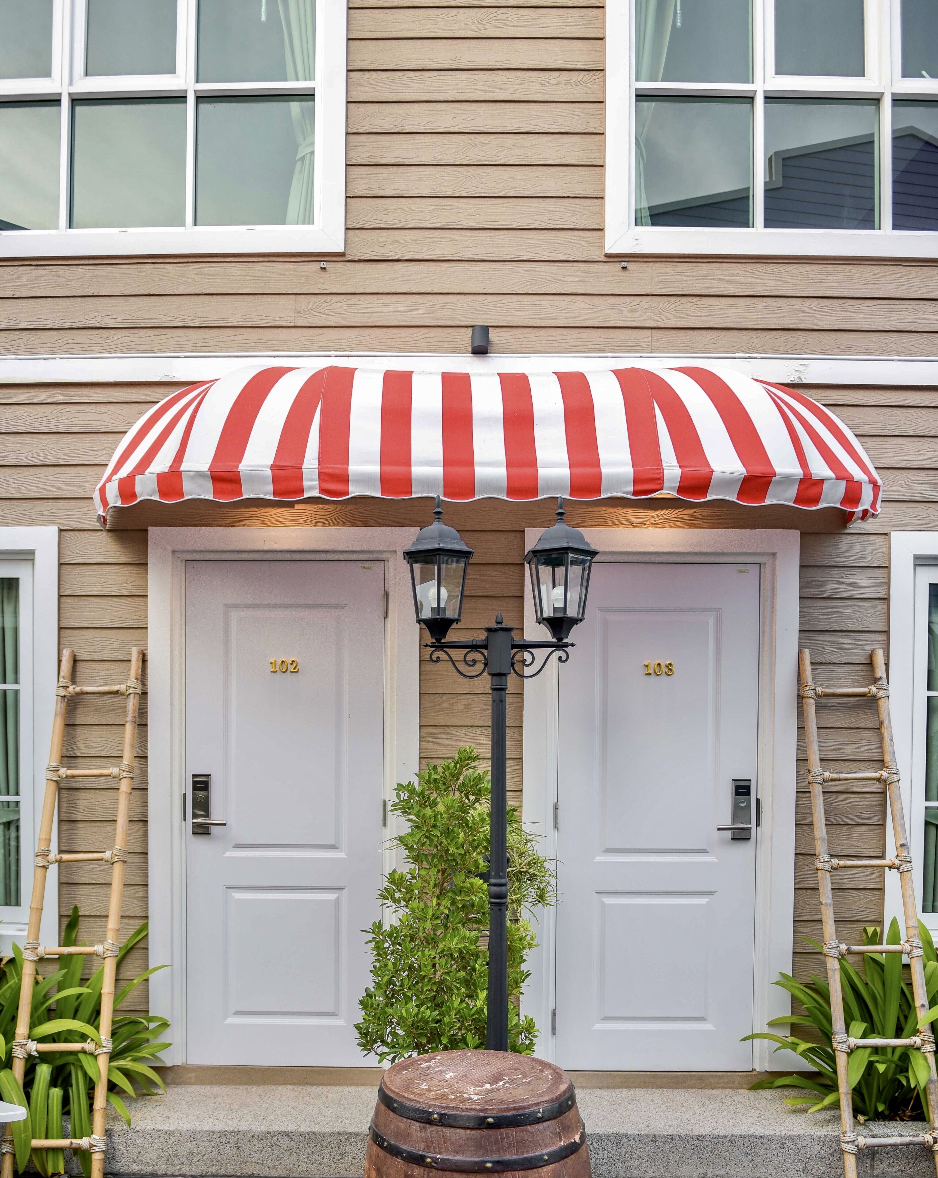 A building with two white doors labeled 102 and 103, a red and white striped awning, and a small tree in front.