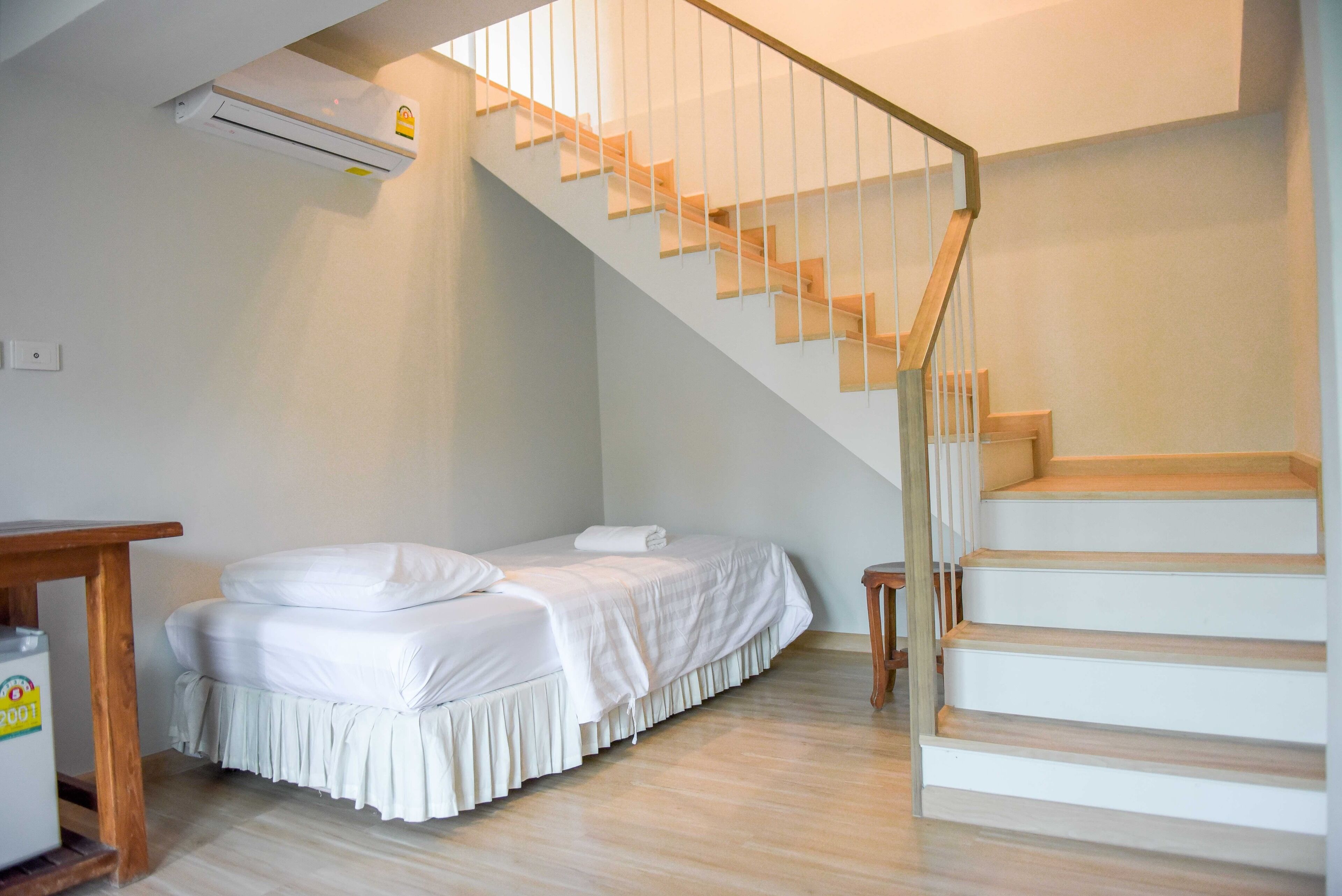 A room with a bed, a wooden table, a small stool, and a staircase.