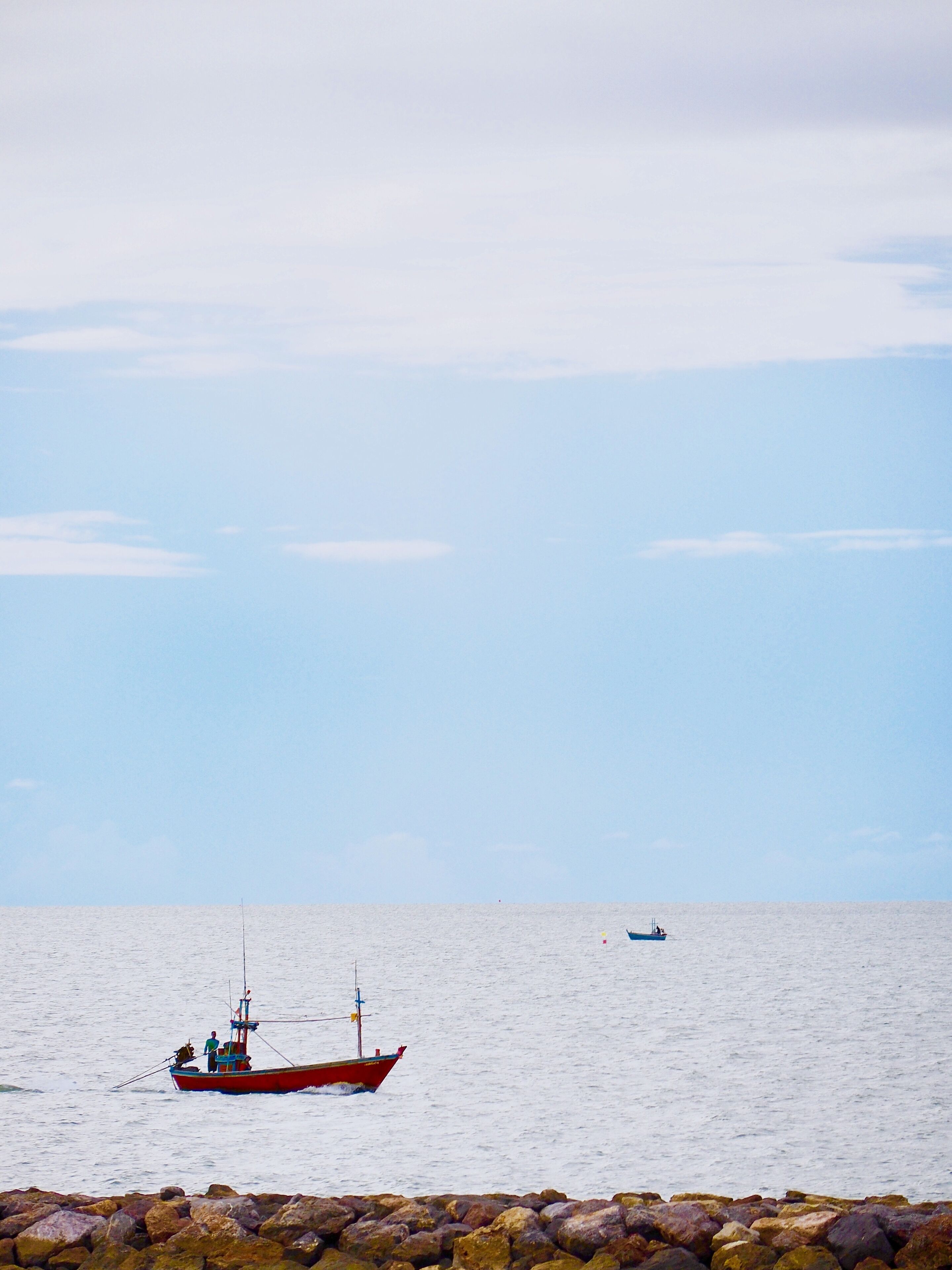 Un bote rojo sobre aguas tranquilas, con una costa rocosa al frente.