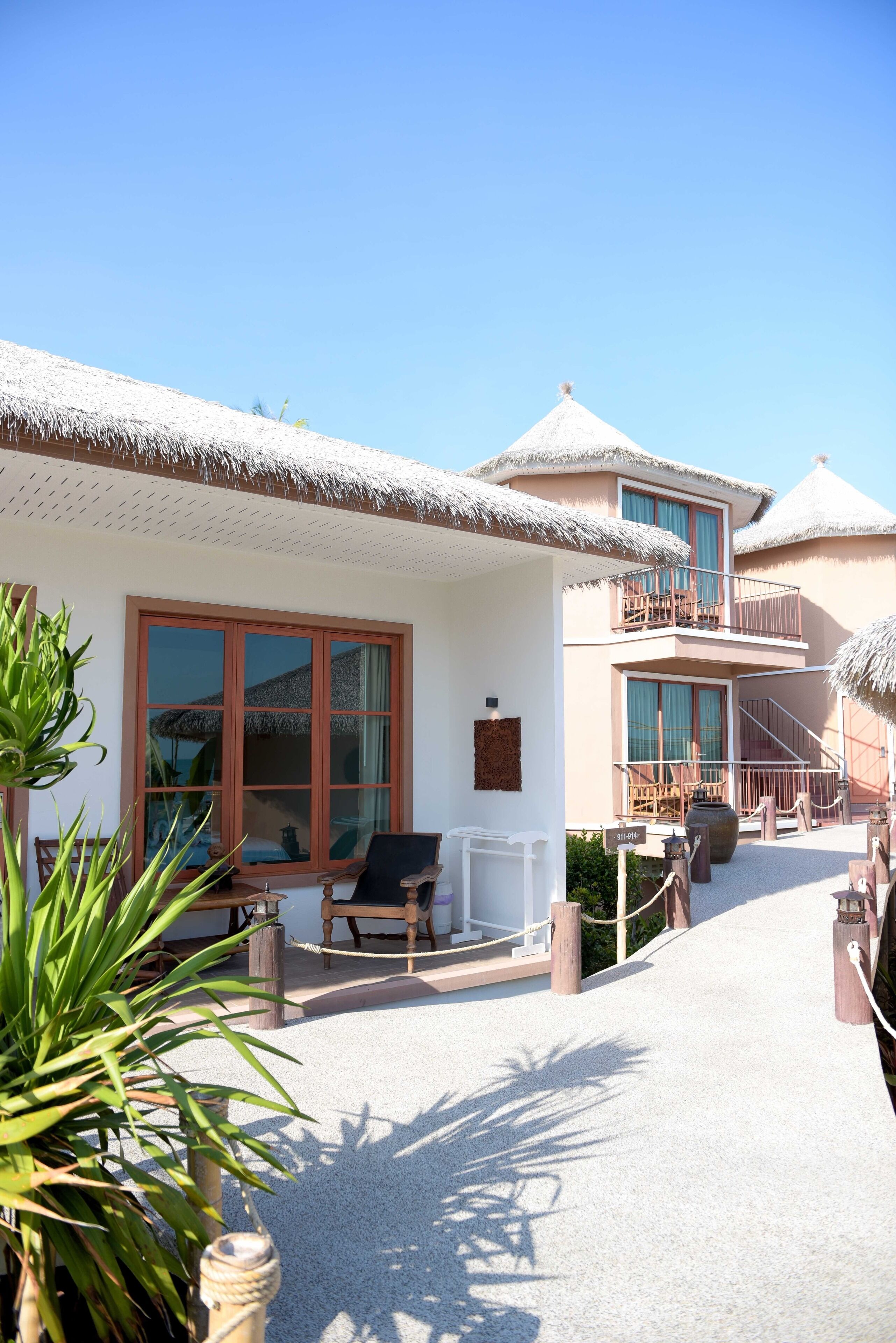 A resort with thatched-roof buildings, a covered outdoor seating area, and a staircase leading to a balcony.