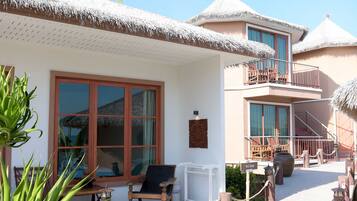 A resort with thatched-roof buildings, a covered outdoor seating area, and a staircase leading to a balcony.