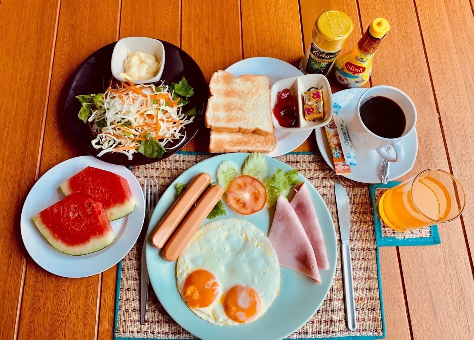 A breakfast setting with plates of food, condiments, and beverages.