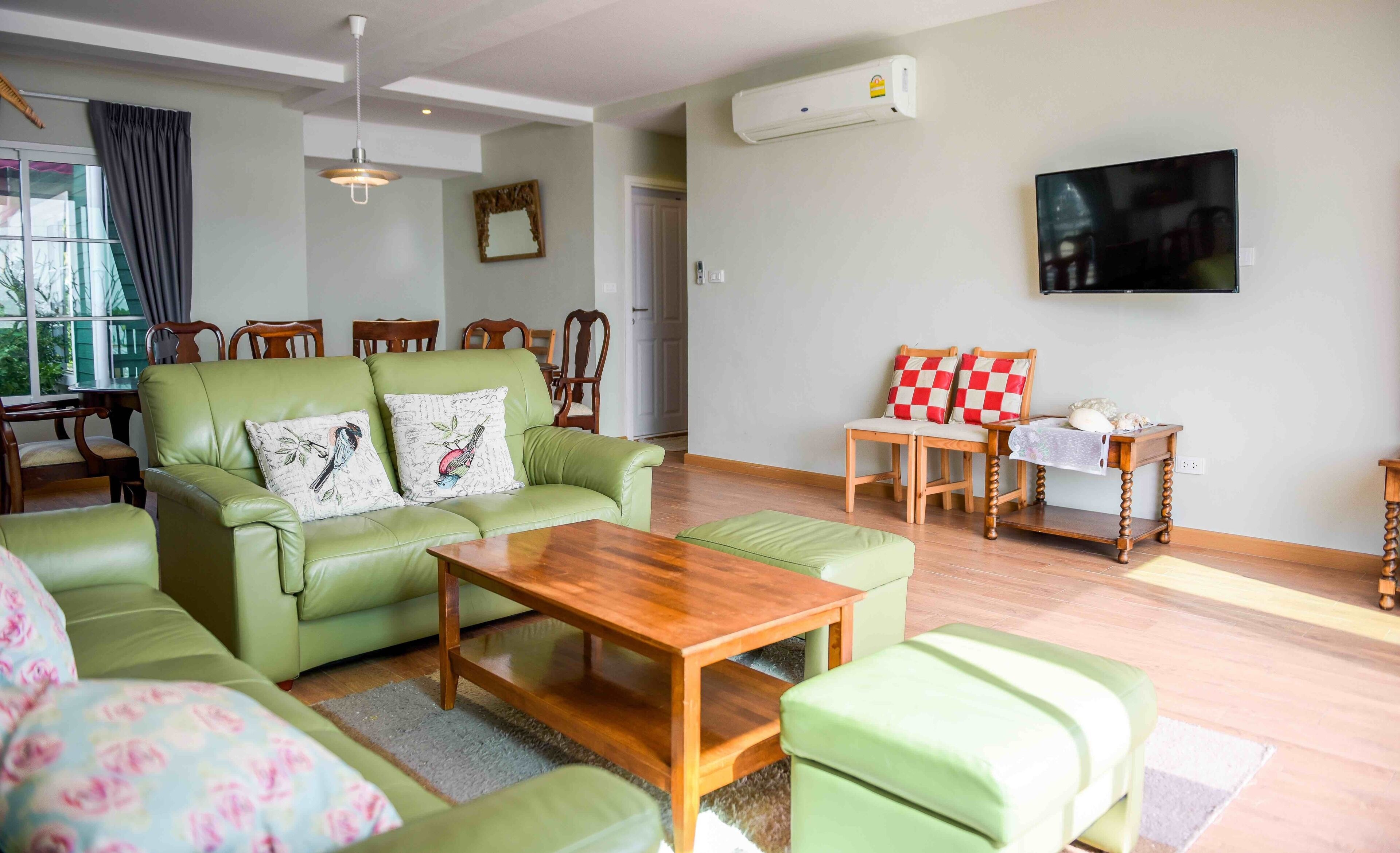 A living room with a green sofa, wooden coffee table, and a TV mounted on the wall.