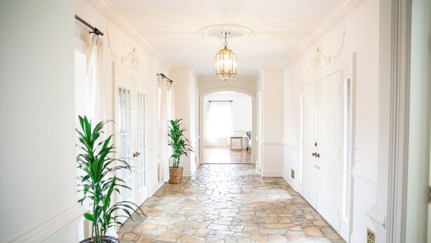 A hallway with stone flooring, white walls, and a chandelier. There are potted plants and doors on either side. - 12-Person House with Hot Tub on Spectacular Estate (Castleton)