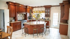 A spacious kitchen with wooden cabinetry, a central island with stools, and a large window providing natural light. - 12-Person House with Hot Tub on Spectacular Estate (Castleton)