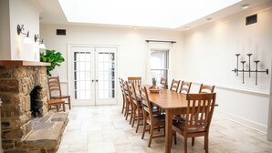 A dining area with a stone fireplace, wooden chairs, a long table, and a view through a glass door. - 12-Person House with Hot Tub on Spectacular Estate (Castleton)