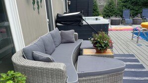 Un espace extérieur aménagé, abrité et doté d’un canapé en osier, d’un jacuzzi et d’une plante en pot.