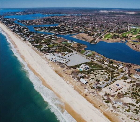 Vista aérea de uma área costeira com praia, edifícios residenciais e corpos d'água.