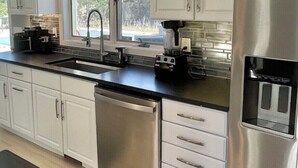 Une cuisine moderne avec des meubles blancs, un lave-vaisselle en acier inoxydable, une machine à café et un réfrigérateur.