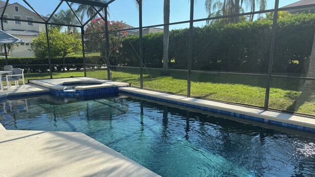 En swimmingpool med krystalklart, blåt vand, omgivet af et glashegn, og et græsareal med træer samt et hus i baggrunden.