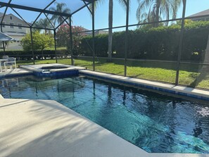 A swimming pool with clear blue water, surrounded by a glass enclosure, and a grassy area with trees and a house in the background. - Orlando vacation rental near to Disney (Davenport)