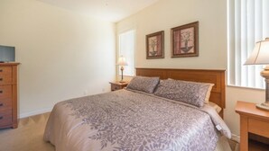 Un dormitorio con una cama grande, cabecera de madera, dos mesitas de noche con lámparas, un aparador de madera y dos cuadros enmarcados en la pared.