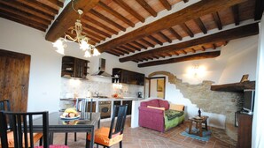 A rustic kitchen with exposed wooden beams, a dining area with a table and chairs, and a cozy living space with a sofa and a television.