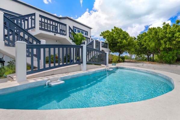 A modern house with a swimming pool, a staircase, and a view of trees.