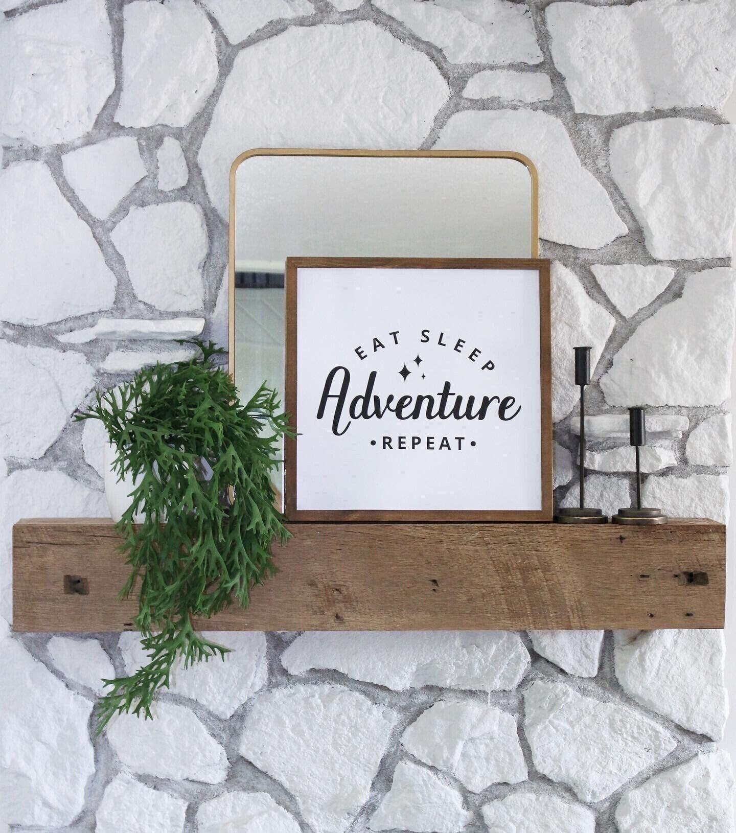 A framed inspirational quote on a wooden shelf against a stone wall.
