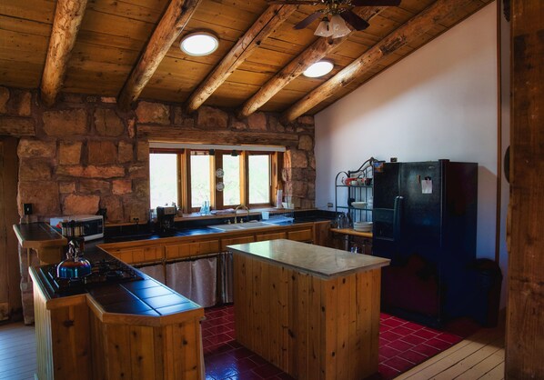 A rustic kitchen with wooden beams, a stone wall, and a large refrigerator.