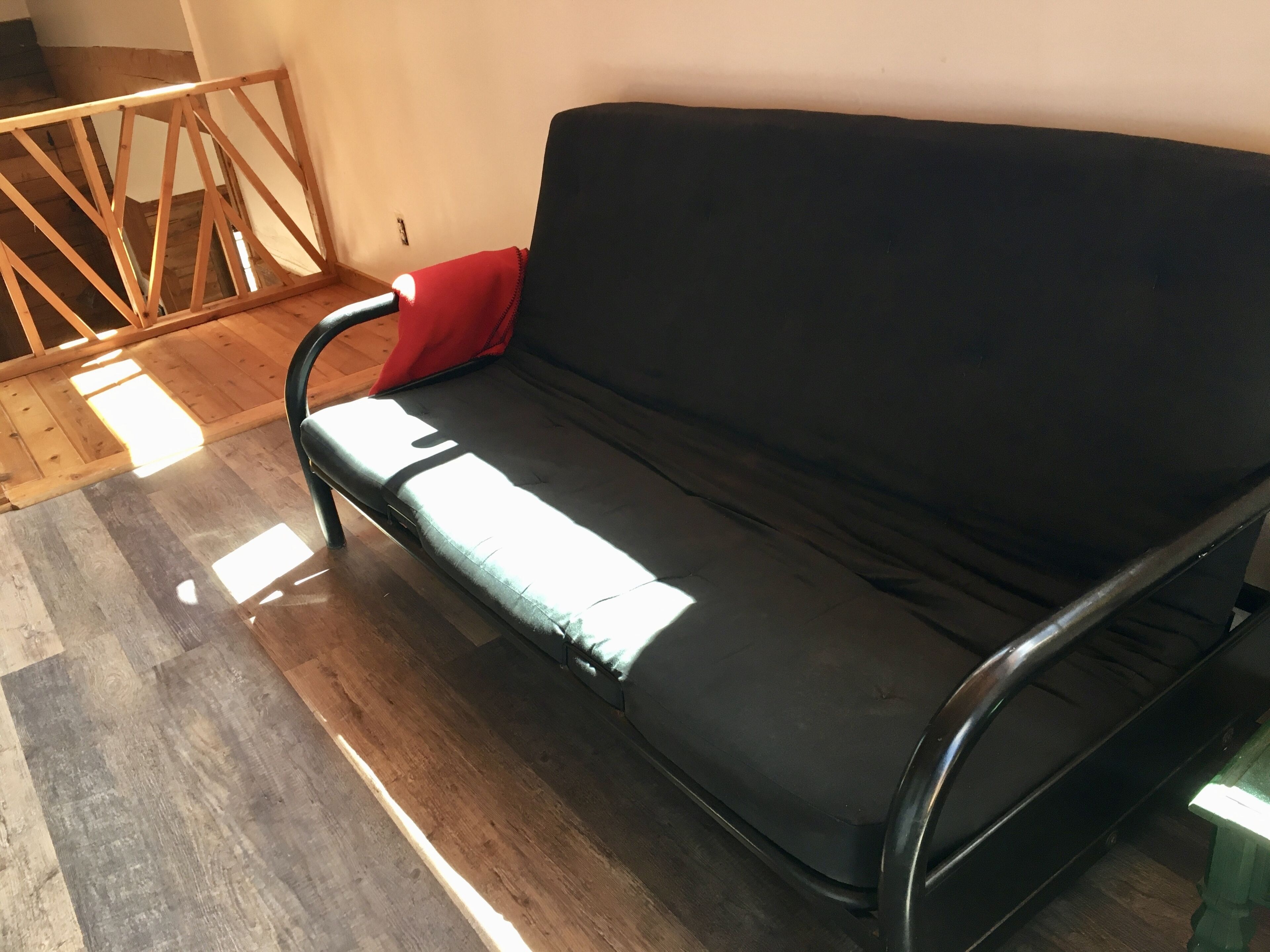 A black sofa with a red cushion in a room with wooden flooring and a wooden railing.