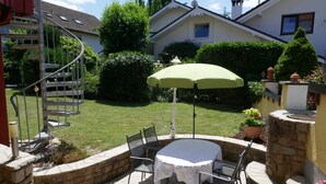 A patio with a round table and chairs, a green umbrella, and a spiral staircase. - Vacation apartment Schwarzwaldliebe near Freiburg, terrace (Bollschweil)