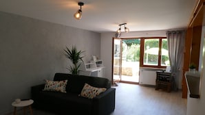 A modern living room with a black sofa, a small side table, a potted plant, and a sliding glass door leading to a balcony. - Vacation apartment Schwarzwaldliebe near Freiburg, terrace (Bollschweil)