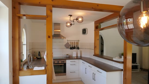 A compact kitchen with white cabinets, a stainless steel stove, and a wooden ceiling structure. - Vacation apartment Schwarzwaldliebe near Freiburg, terrace (Bollschweil)