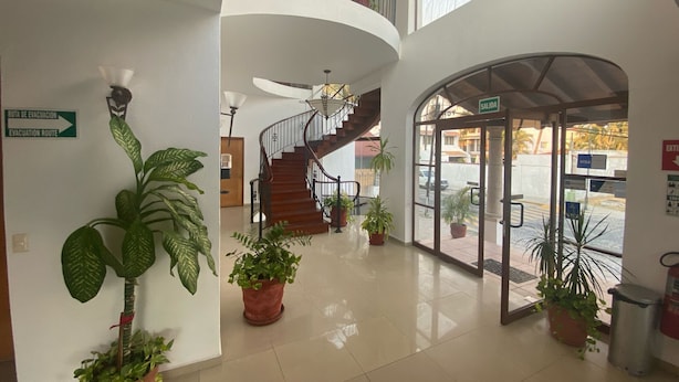 A spacious lobby with a curved staircase, potted plants, and a clear evacuation route sign. - Hotel Pez Vela Manzanillo (Manzanillo)