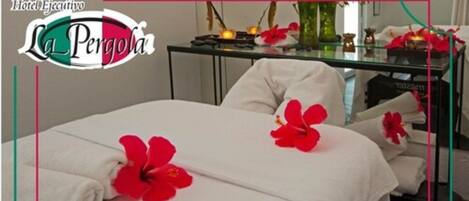 Habitación de hotel con cama, almohadas, una mesita de vidrio con un florero y una pequeña estatua.