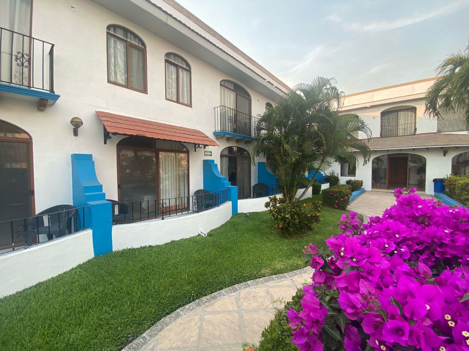 Un edificio de dos pisos con fachada blanca, detalles azules y un patio con baldosas.