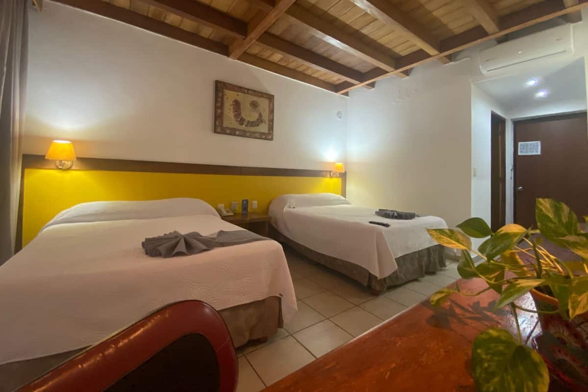 Une chambre d’hôtel avec deux lits, un plafond en bois, une lampe fixée au mur et une porte.