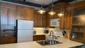 A kitchen with wooden cabinets, a white refrigerator, a microwave, a stove, and a sink with a modern faucet. There are three pendant lights above the sink.