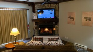A cozy room with a stone fireplace, a television mounted above it, and a comfortable sofa with plaid cushions.
