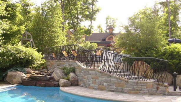 A swimming pool with a stone and metal deck, surrounded by lush greenery and trees.