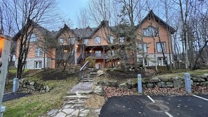 A large, multi-story building with a stone facade, multiple windows, and a central staircase leading to a porch.