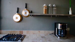 A kitchen with a gas stove, two hanging pots, a coffee maker, and spice jars on a shelf. - 50% of Monthly 35% weekly  (Versalles)