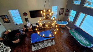 A room with a pool table, a chandelier, a bar area, and a large window.