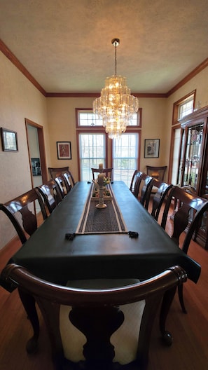 A dining room with a long table, chairs, a chandelier, and large windows.