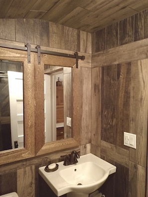 Un baño con paneles de madera, un lavamanos blanco y un espejo grande.