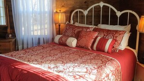 A wooden cabin bedroom with a bed, curtains, and a nightstand.
