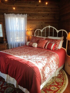 Un dormitorio de cabaña de madera con cama, cortinas y mesita de noche.