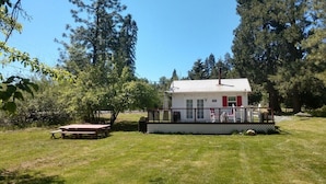 A small house with a porch, surrounded by trees and a grassy yard.