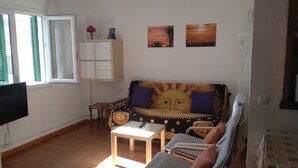 A living room with a sofa, a small table, a TV, a cabinet, and two wall-mounted pictures. - Apartment 100 meters from the promenade and beach. Incredible rooftop views. (Conil de la Frontera)