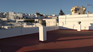A rooftop terrace with a view of a cityscape, featuring white buildings and a castle-like structure in the distance. - Apartment 100 meters from the promenade and beach. Incredible rooftop views. (Conil de la Frontera)