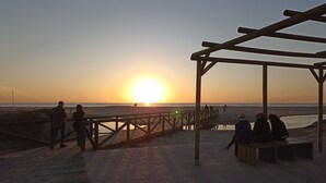 A wooden pier extending over a sandy beach with people walking and sitting under a wooden pergola. - Apartment 100 meters from the promenade and beach. Incredible rooftop views. (Conil de la Frontera)