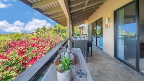 Une terrasse extérieure avec une table à manger, un jardinier orné de fleurs rouges et une vue sur l’océan.