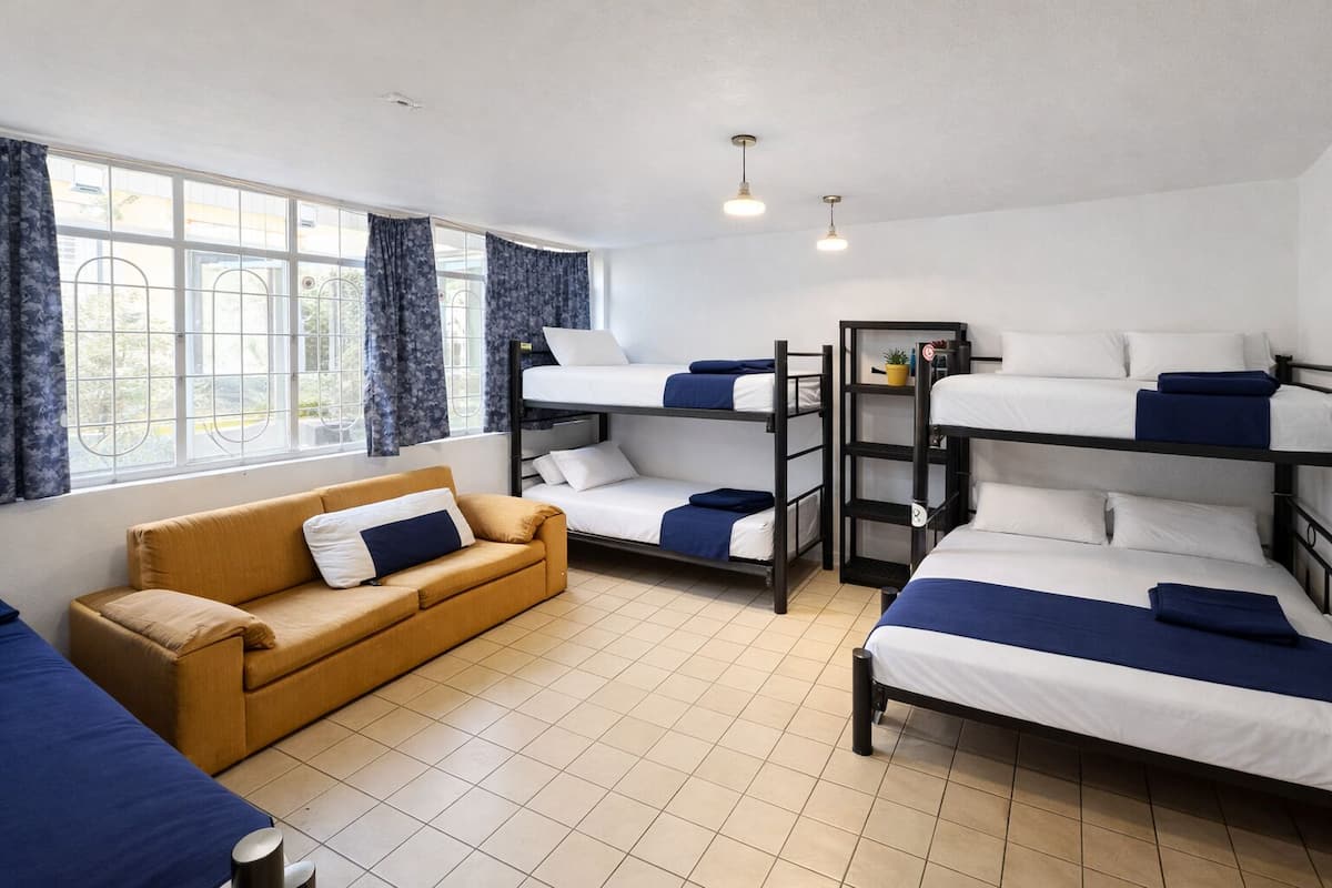 A dormitory room with bunk beds, a sofa, and a window with curtains.