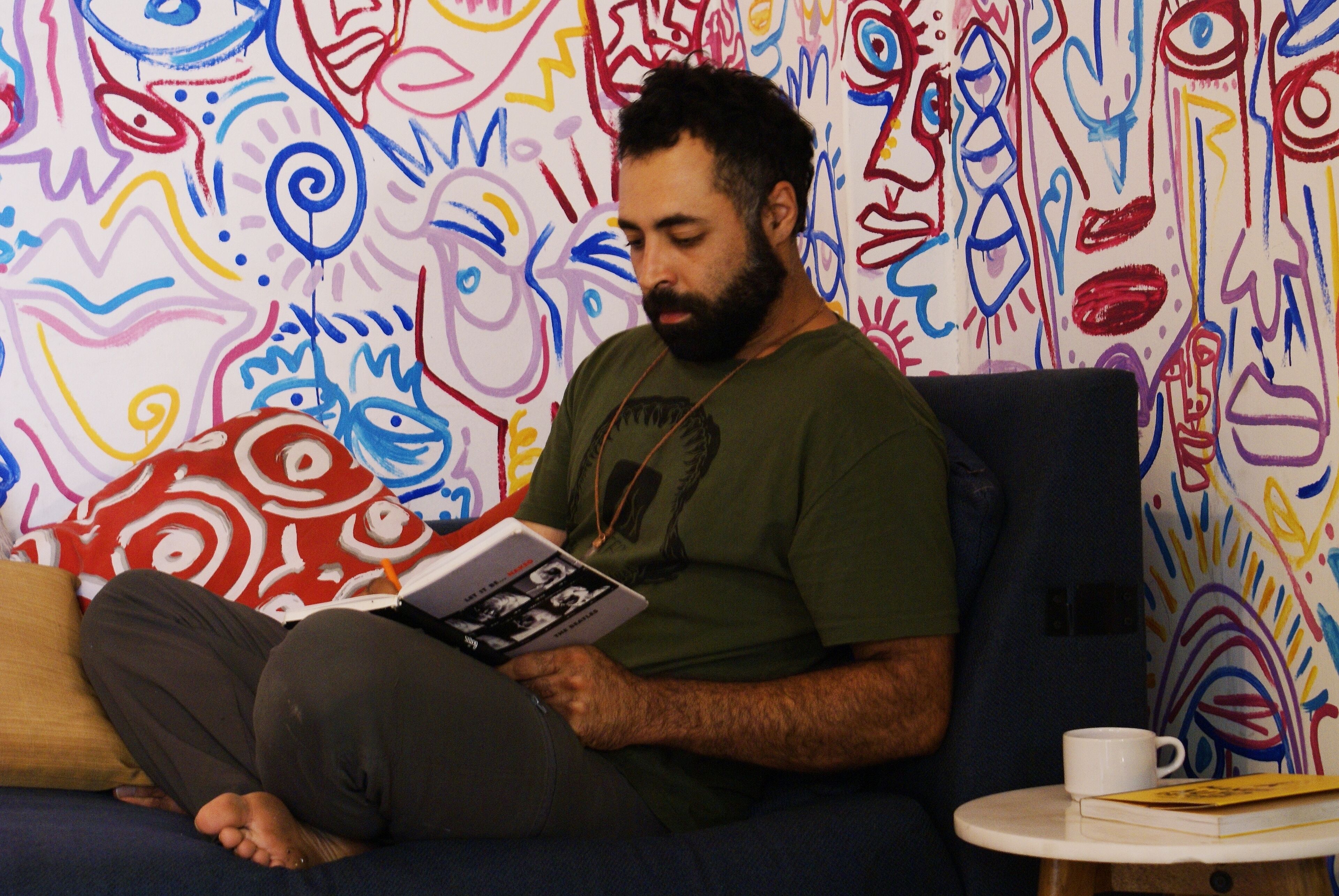 A person sitting on a couch reading a book in a room with colorful abstract wall art.